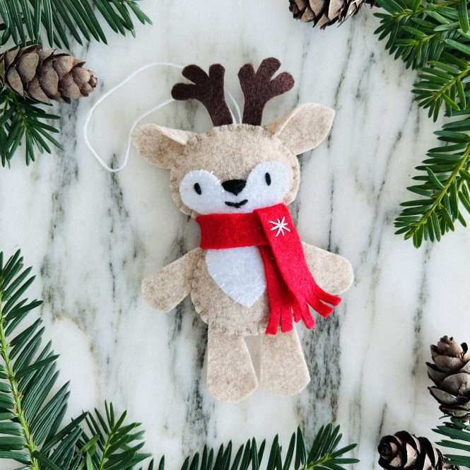 hand stitched felt reindeer ornament stuffie surrounded by pine branches and pine cones