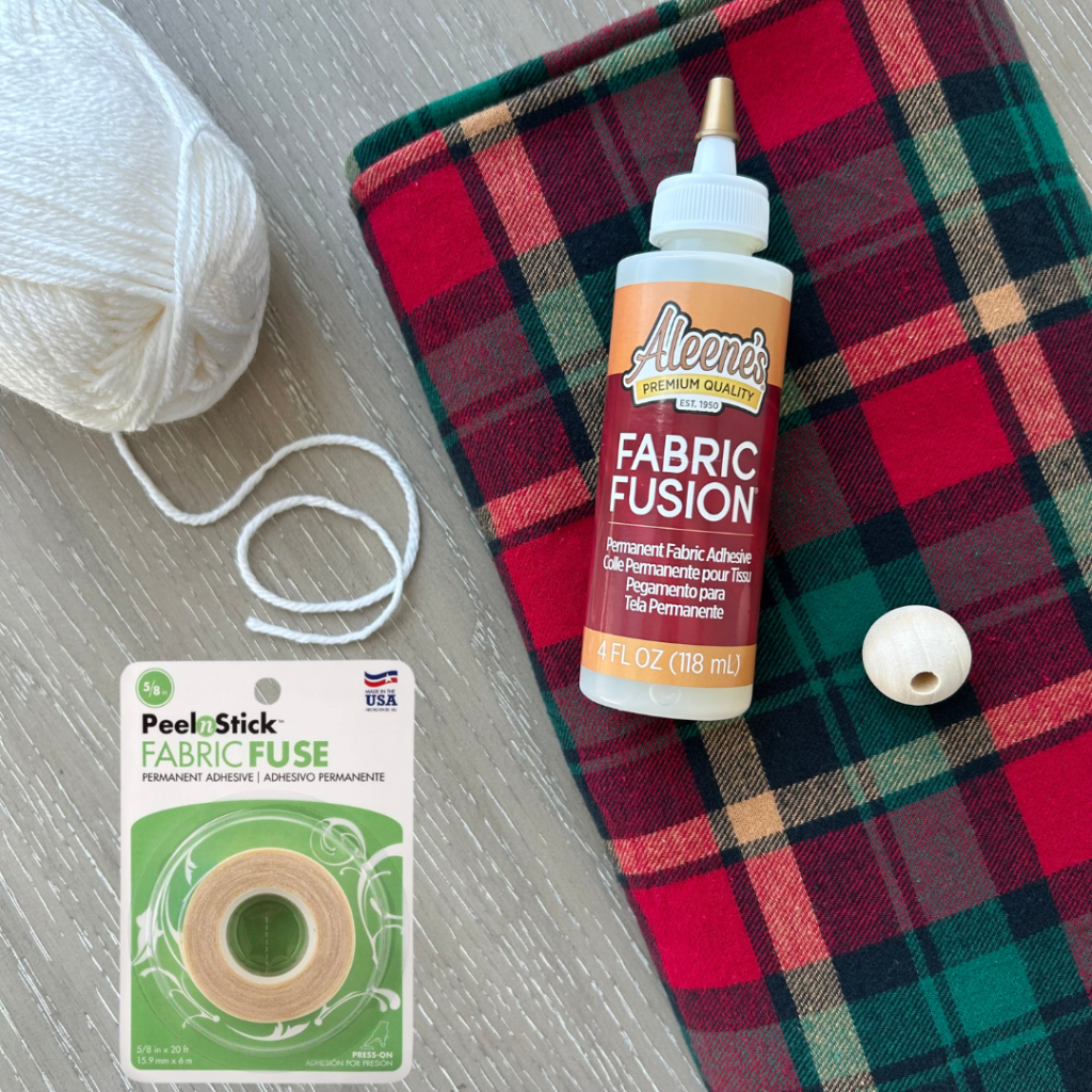 Supplies to make a gnome without sewing - Aleene's Fabric Fusion Adhesive and Thermoweb Peel n Stick Fabric Fuse tape, along with red plaid flannel, whit yarn and a wooden bead.