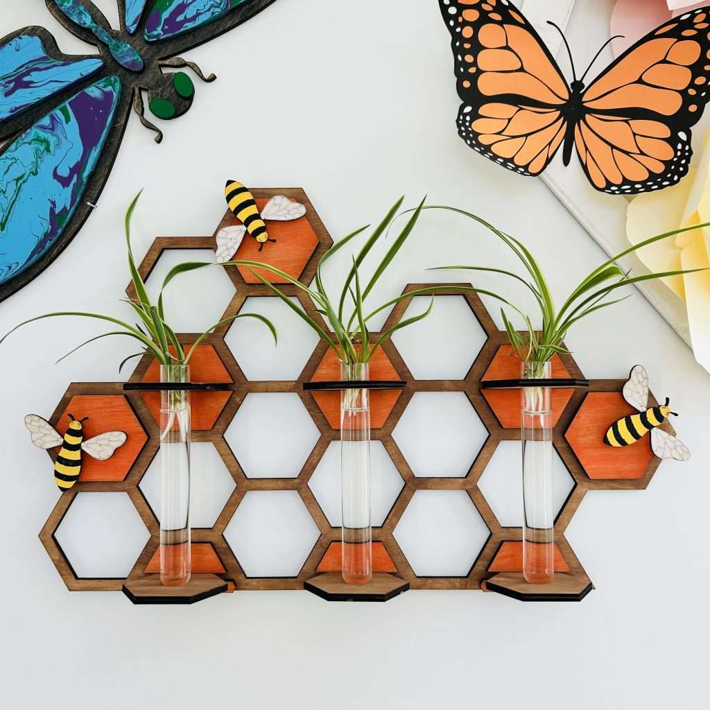 Buzz and Grow Plant Propagation Station. Wooden honeycomb with 3 test tubes holding spider plant pups for propagation. Also has painted wooden bees attached to honeycomb for decoration.