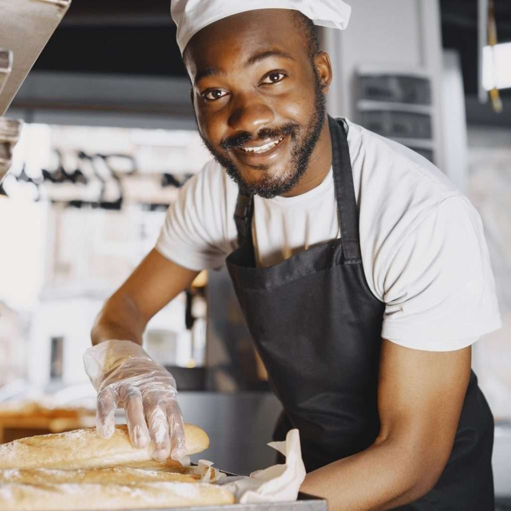 Man wearing a chefs hat, gloves and apron, working in a kitchen